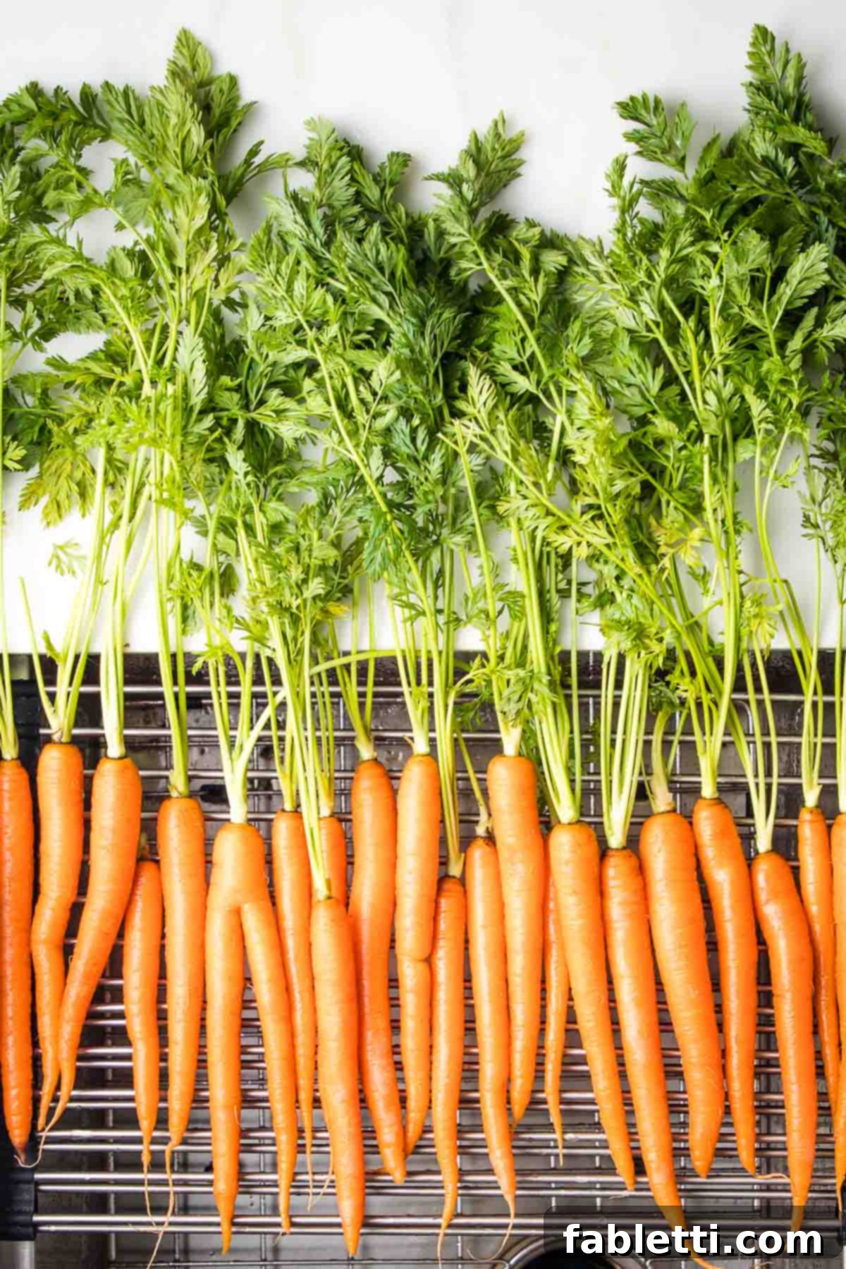Carrots with carrot greens drying on a metal rack.