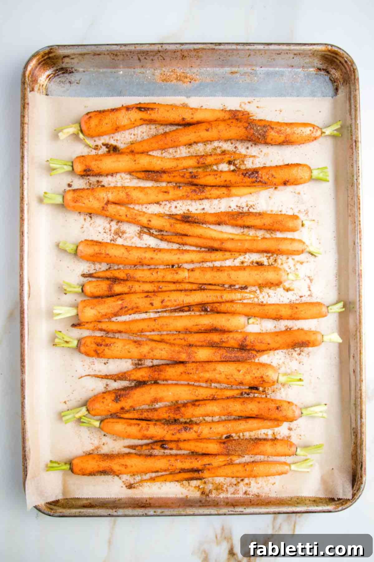 Whole carrots rubbed in spices on a rimmed baking tray lined with parchment.