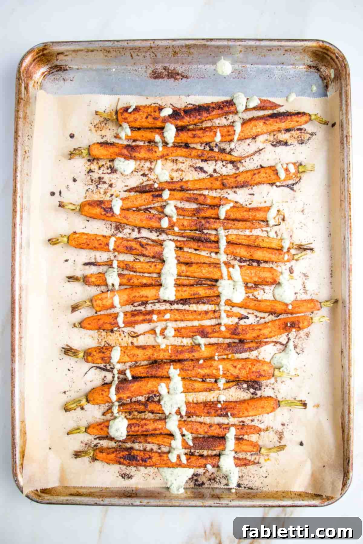 Roasted carrots on a parchment lined baking tray, drizzled with lemon tahini