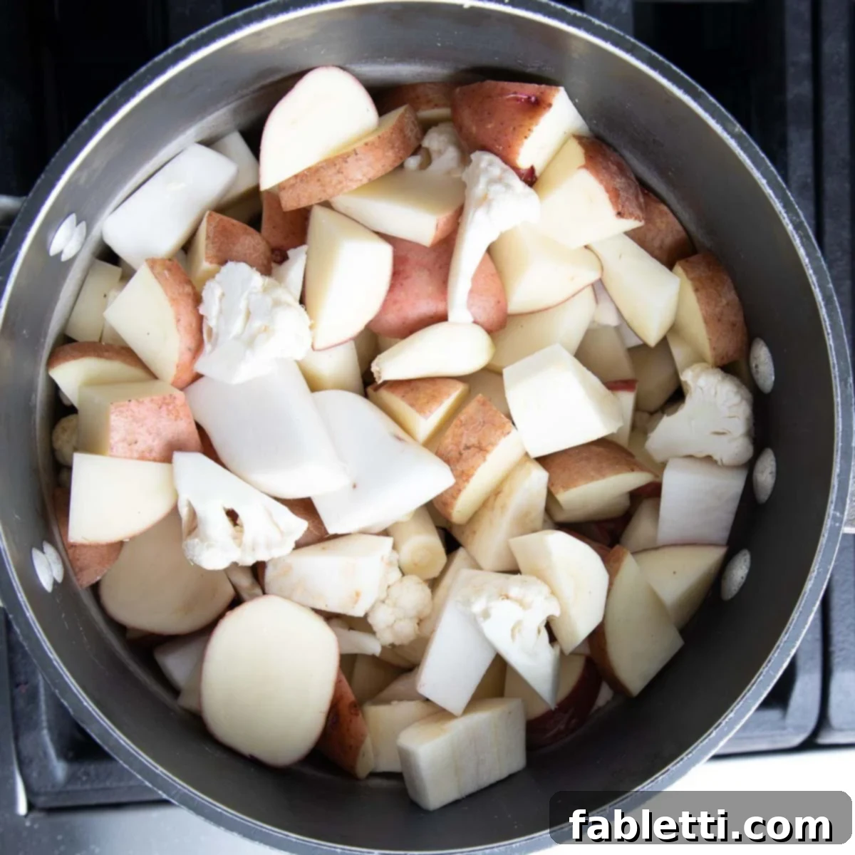 Heavenly Dairy-Free Garlic Mash 4 A large pot filled with cubed potatoes, peeled garlic cloves, chopped parsnips, turnips, and celery root, ready for cooking.