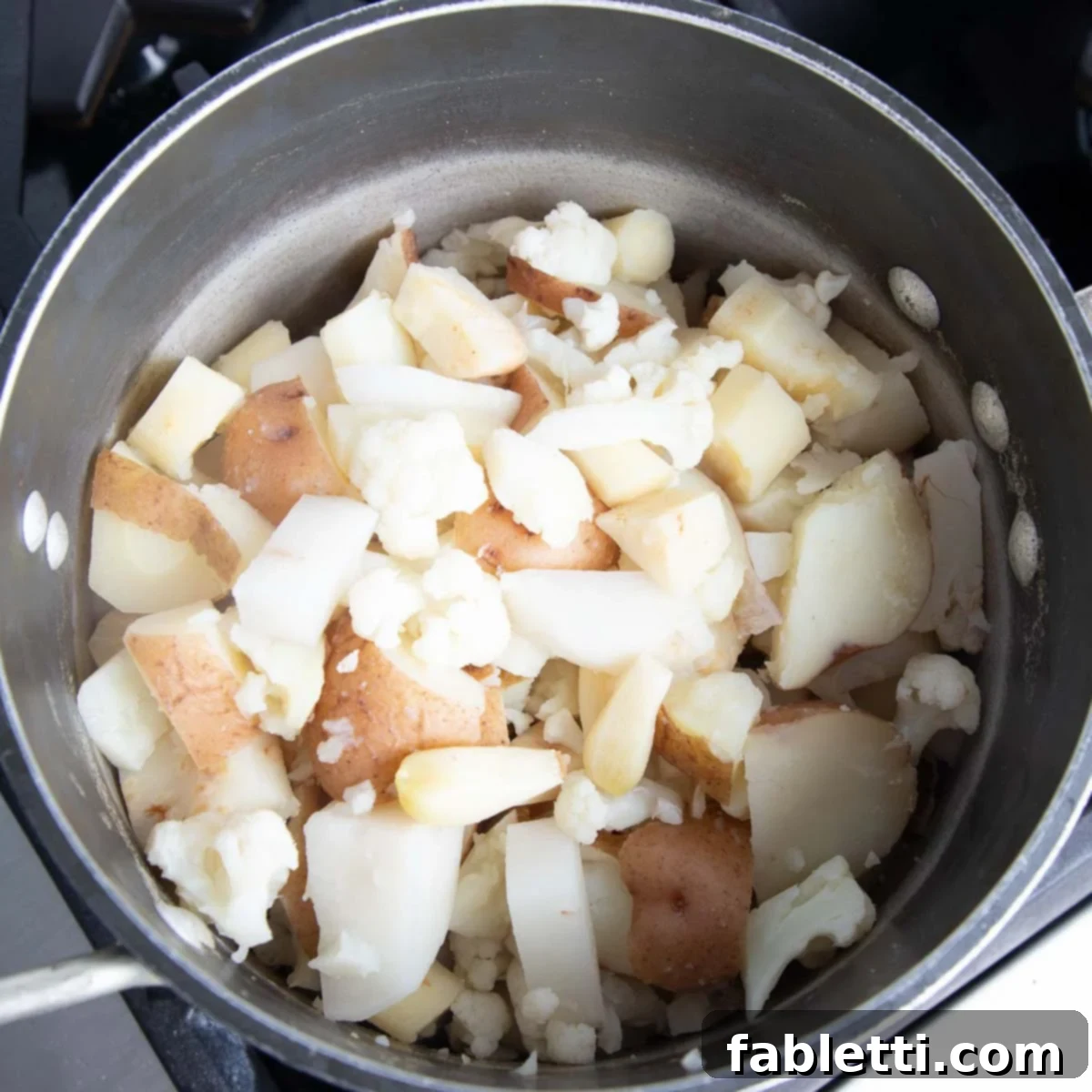 Heavenly Dairy-Free Garlic Mash 6 A close-up of tender, cooked white root vegetables and cauliflower chunks in a large pot after draining.