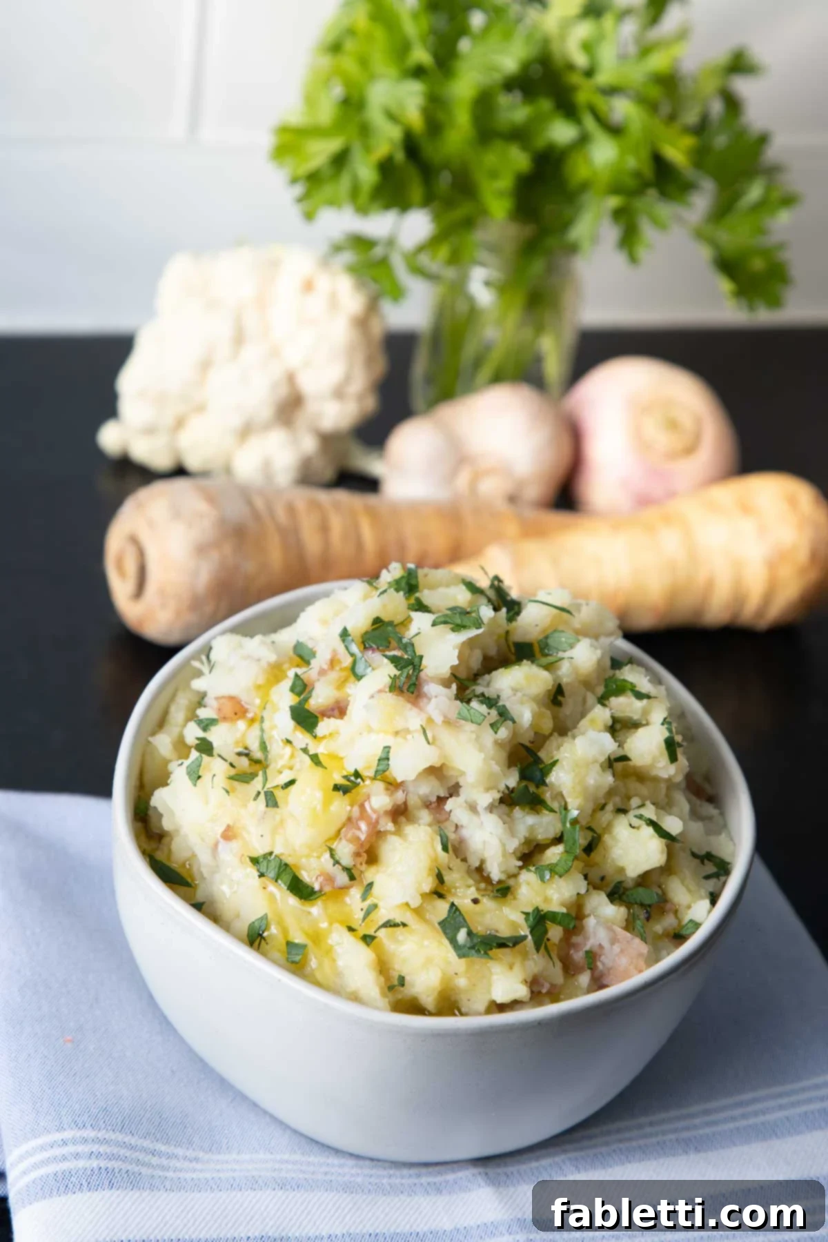 Heavenly Dairy-Free Garlic Mash 9 A beautifully presented bowl of creamy mashed potatoes, garnished with fresh green herbs, with blurred root vegetables in the background, suggesting wholesome ingredients.