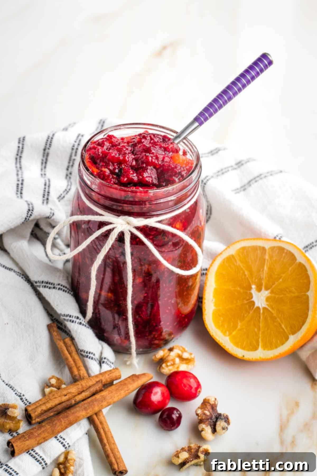 Refined Sugar-Free Cranberry Sauce 12 A close-up of a small glass bowl filled with vibrant homemade cranberry sauce, garnished with fresh cranberries, orange peel, and cinnamon sticks, highlighting its rich texture and inviting aroma.