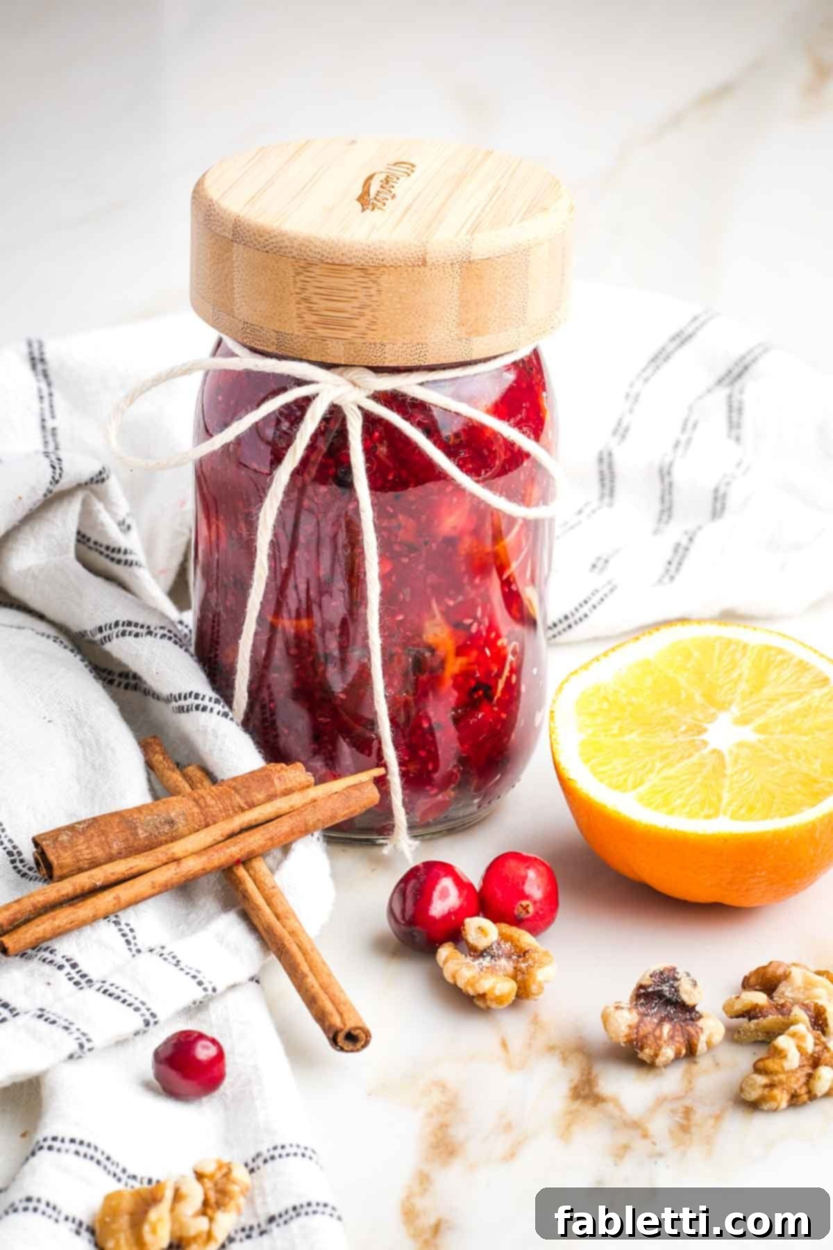Refined Sugar-Free Cranberry Sauce 13 A neatly arranged group of three small mason jars filled with luscious homemade cranberry sauce, ready for storage or gifting, surrounded by a few stray cranberries and a cinnamon stick.