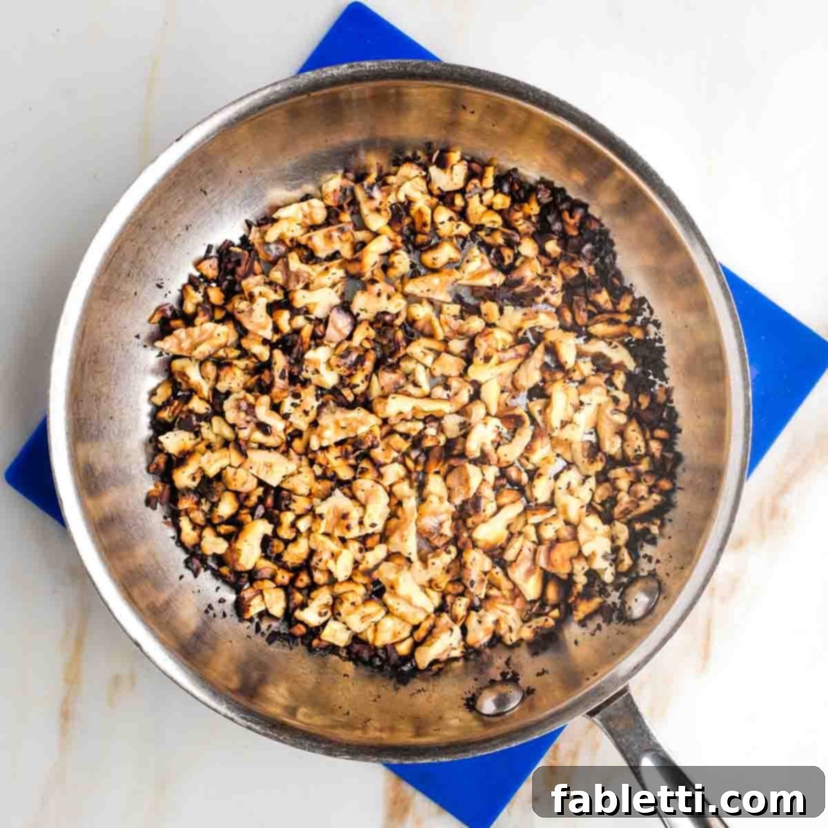 Refined Sugar-Free Cranberry Sauce 8 A small skillet on the stovetop filled with coarsely chopped walnuts, lightly toasting to a golden brown, indicating they are nearly ready to be added to the cranberry sauce.