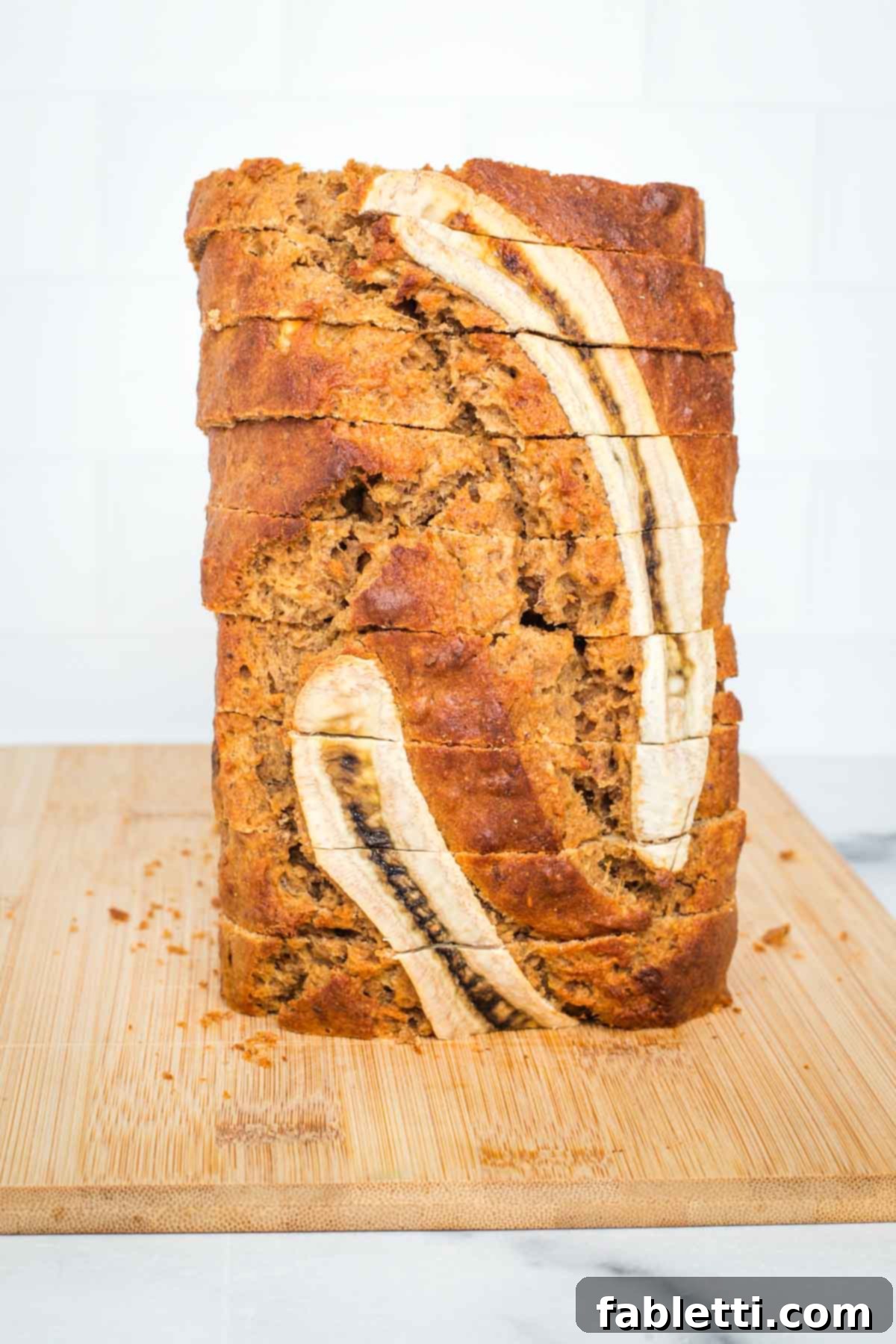 Thickly sliced Maple Miso Banana Bread, stacked vertically to showcase its moist interior and a decorative banana slice on top.