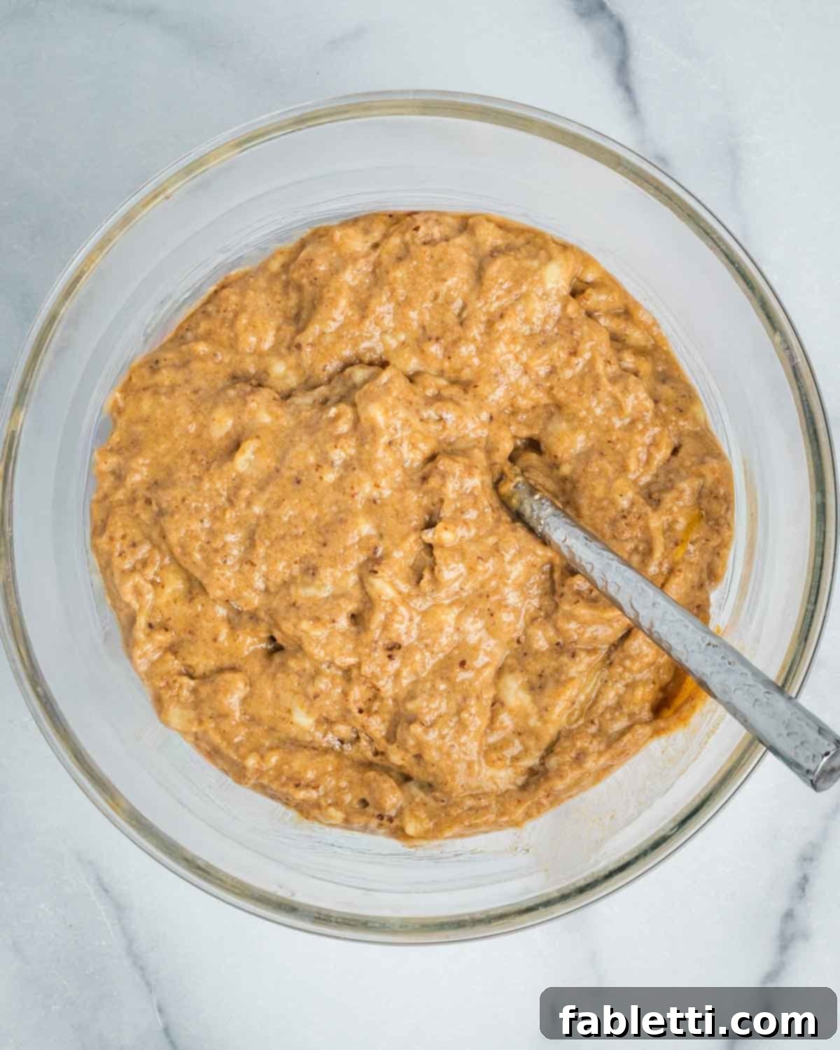 Banana bread batter in a mixing bowl, just combined with a fork, showing its uniform but slightly lumpy texture before baking.