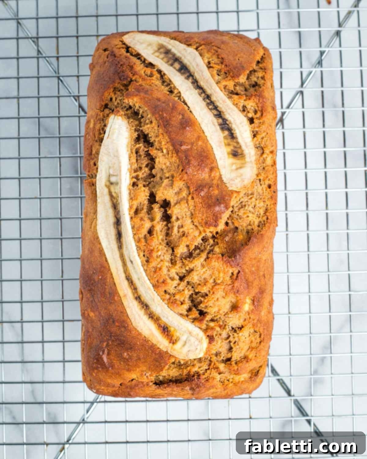 A freshly baked loaf of crisp-top banana bread, resting on a wire rack to cool after being removed from the pan.