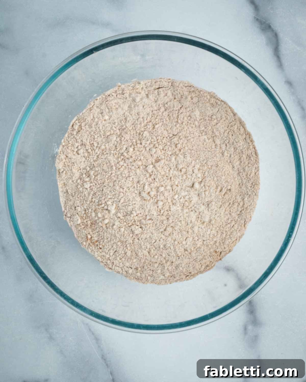 The dry ingredients for banana bread, including flour, ground flax, cinnamon, and baking powder, have been thoroughly mixed together in a glass bowl.