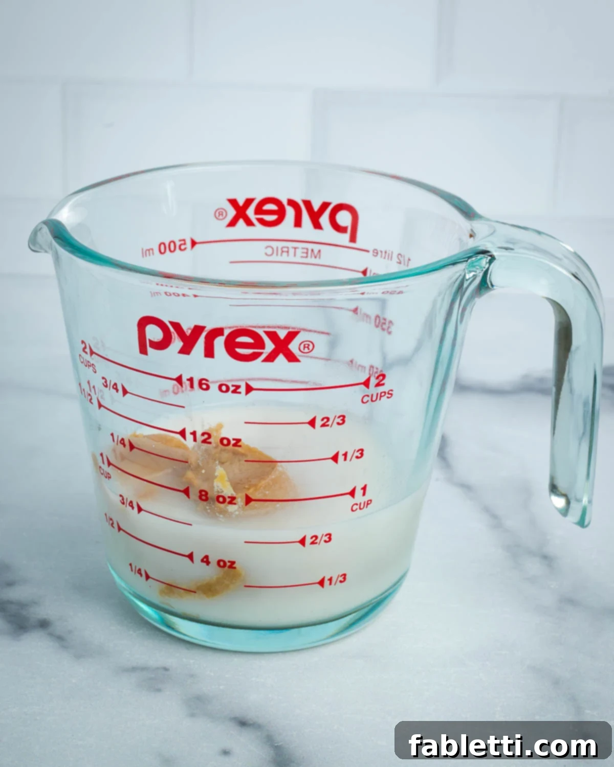 Light miso paste being added to almond milk in a glass measuring cup, ready to be mixed.
