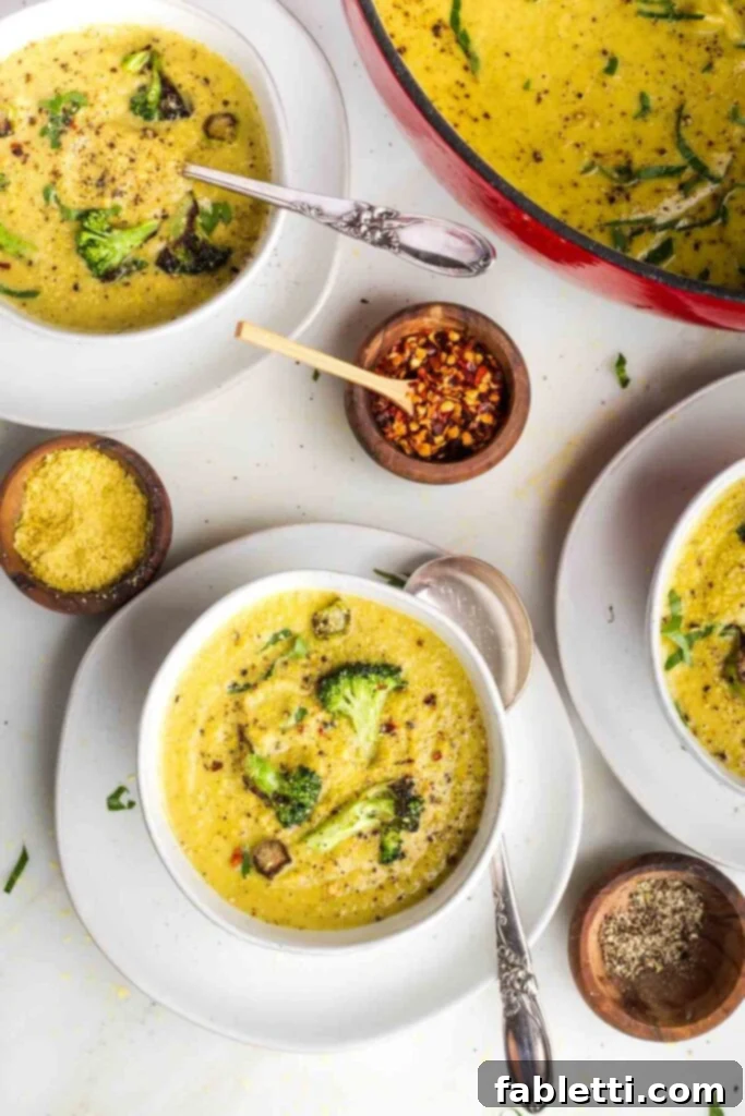 Velvety Plant-Based Broccoli Soup 2 Bowls of creamy yellow soup with chunks of crispy broccoli and pepper floating on the surface.