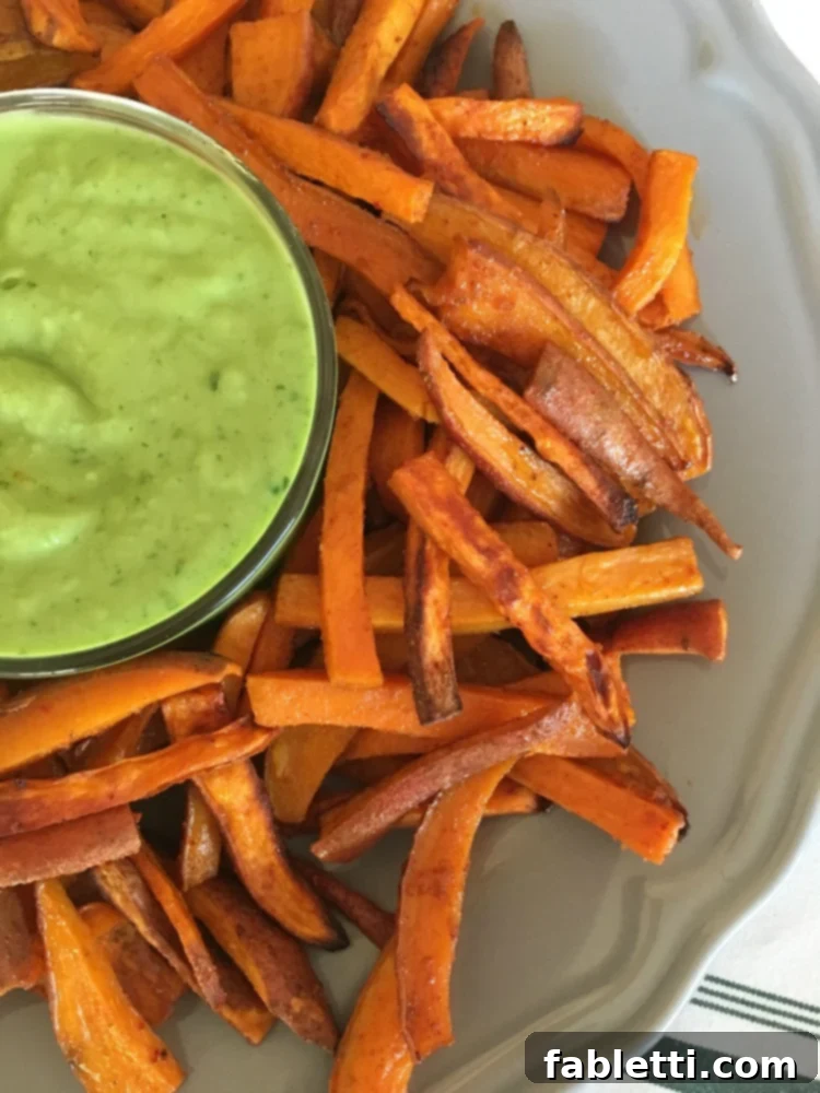 Golden Crispy Sweet Potato Fries 2 Crispy sweet potato fries on a grey plate with a dish of avocado dressing in the center.