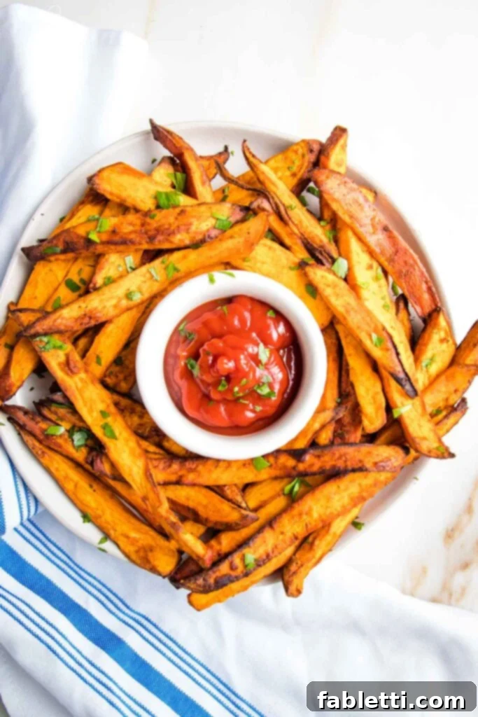 Golden Crispy Sweet Potato Fries 11 Plate of sweet potato fries sprinkled with fresh herbs, with a small dish of ketchup in the center.
