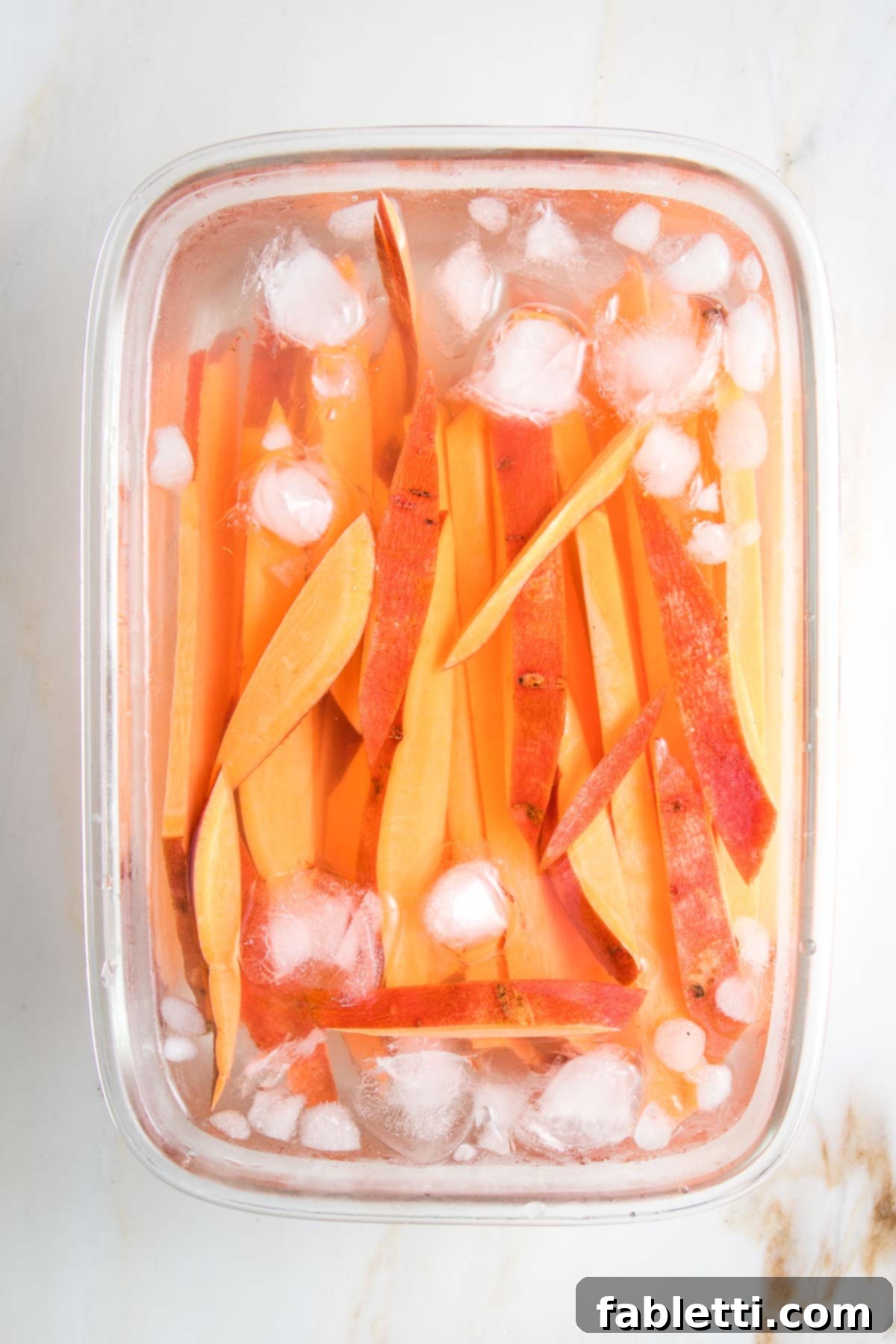 Golden Crispy Sweet Potato Fries 7 Slices of sweet potatoes soaking in ice water.