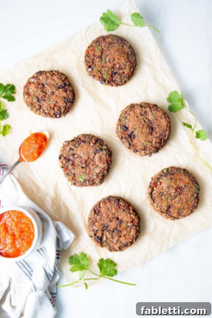 Plant-Powered Black Bean Burgers 2 Parchment paper with freshly baked veggie burgers and a bowl of bright red roasted red pepper sauce ready to be spooned on top.