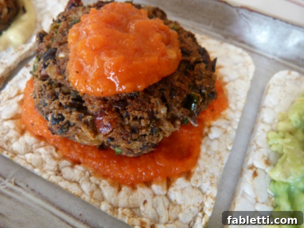 Plant-Powered Black Bean Burgers 12 A mini black bean veggie burger generously layered with vibrant red pepper sauce, both underneath and on top, creating a visually appealing and flavorful slider.