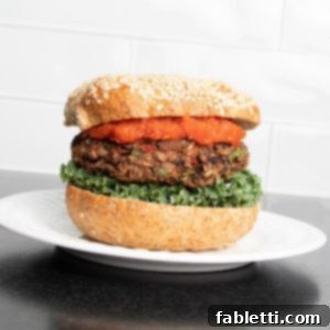 Plant-Powered Black Bean Burgers 13 A delicious veggie burger on a sesame bun, topped with fresh lettuce and a generous drizzle of vibrant red sauce, served on a white plate.