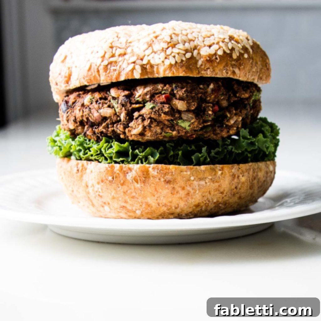 Plant-Powered Black Bean Burgers 3 A perfectly assembled black bean veggie burger served on a toasted sesame seed bun with crisp green lettuce and a dollop of red sauce.