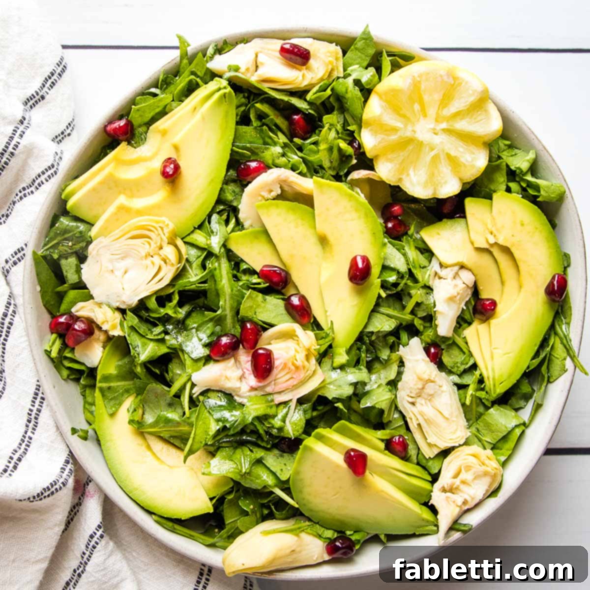 Vibrant Arugula & Lemon Salad 11 A vibrant arugula salad finished with delicate avocado slices, tender artichoke hearts, bright pomegranate seeds, and a wedge of fresh lemon, ready to be served.