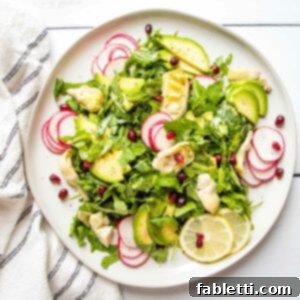 Vibrant Arugula & Lemon Salad 13 Large rimmed white plate with lemony arugula salad. Thinly sliced radish, quartered artichoke hearts, thinly sliced avocado plus pomegranate seeds and lemon slices decorate the simple salad.