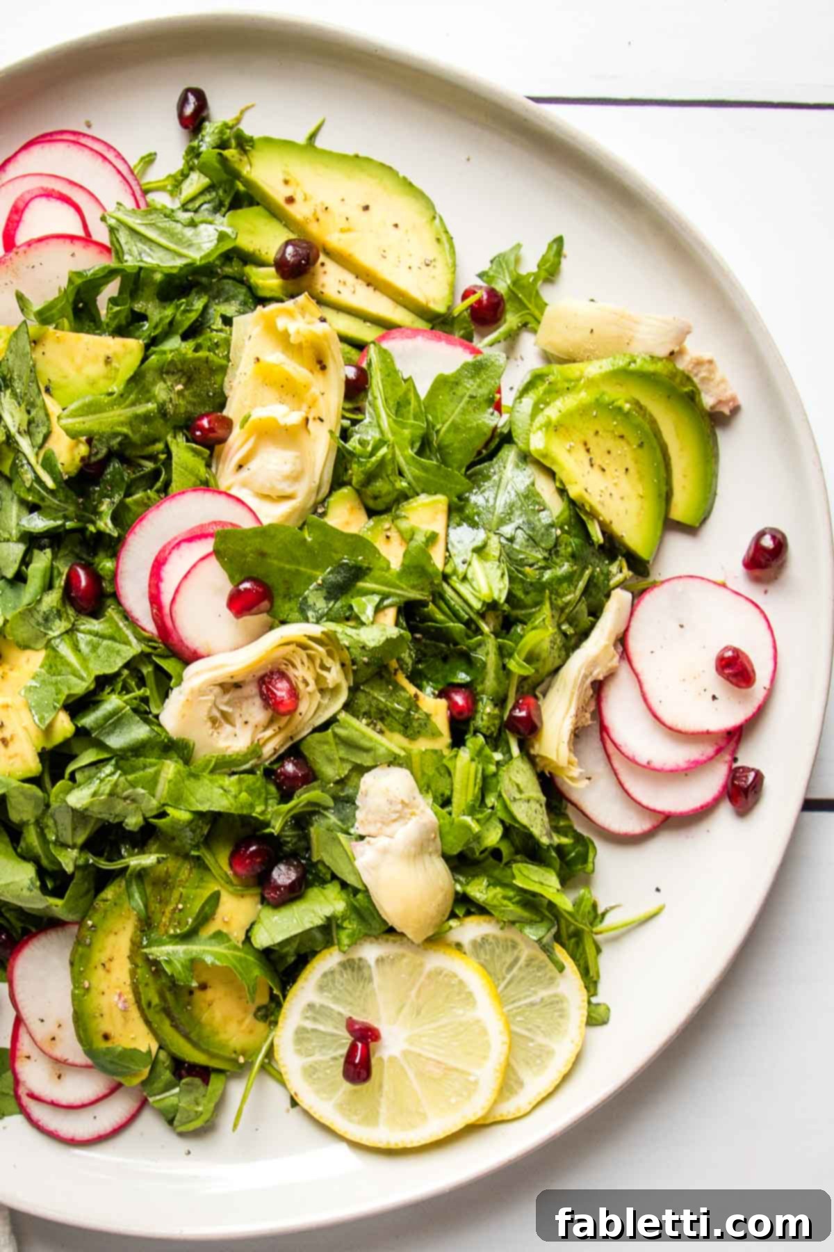 Vibrant Arugula & Lemon Salad 3 Composed salad with arugula, perfectly ripe avocado, tender artichoke hearts, and thinly sliced radishes, all adorned with a sprinkle of glistening pomegranate seeds.