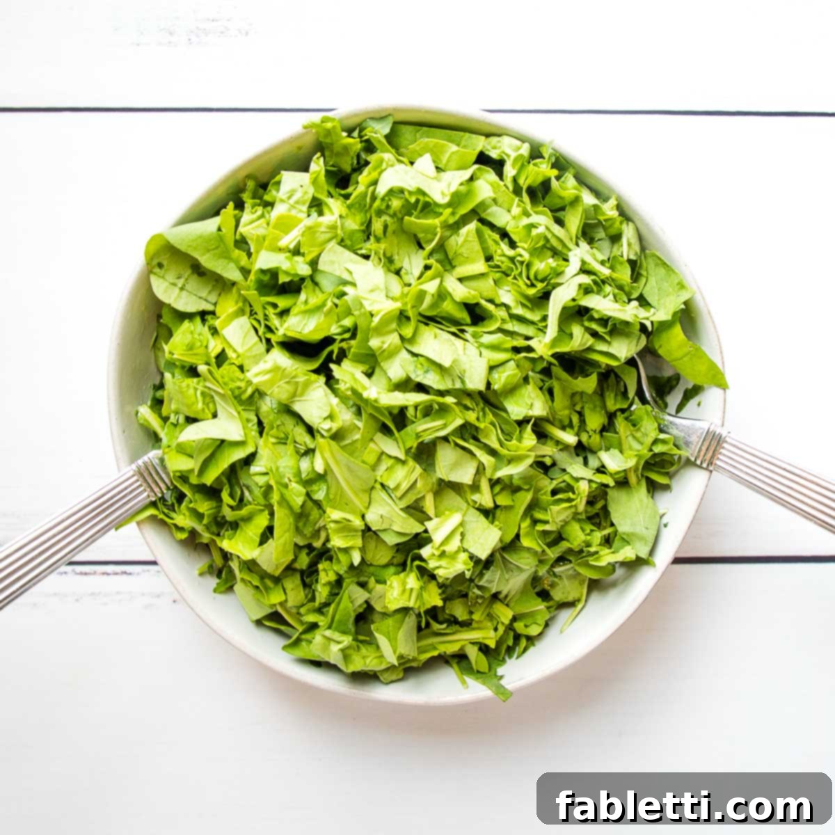 Vibrant Arugula & Lemon Salad 8 Freshly washed arugula leaves are gently placed into a large white bowl, ready to be tossed with the prepared dressing, alongside shiny silver salad tossers.