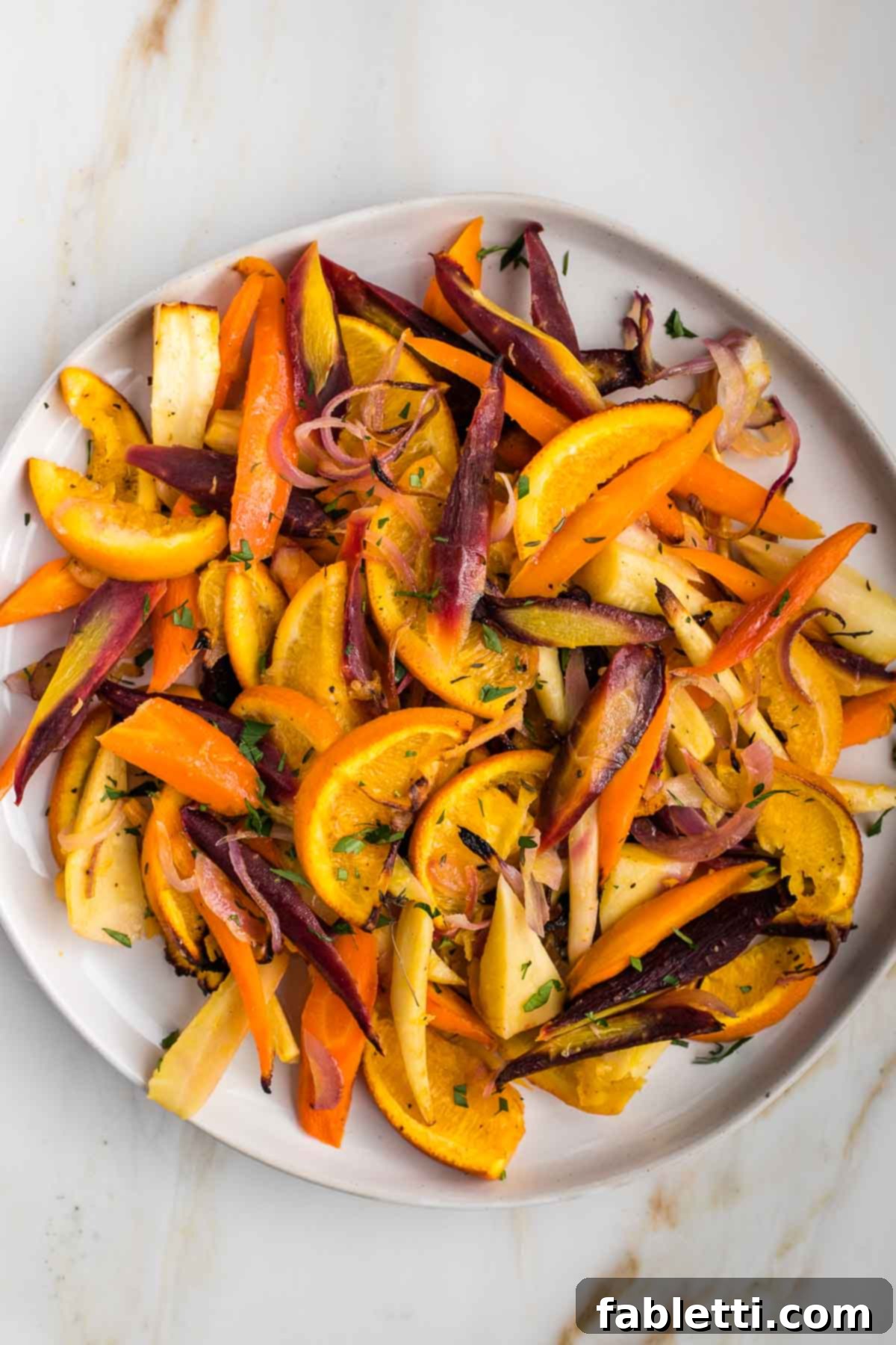 Nectar-Kissed Roasted Roots 2 Brightly colored roasted root vegetables, purple and orange carrots, onions, parsnips and oranges arranged on a rustic wooden board.