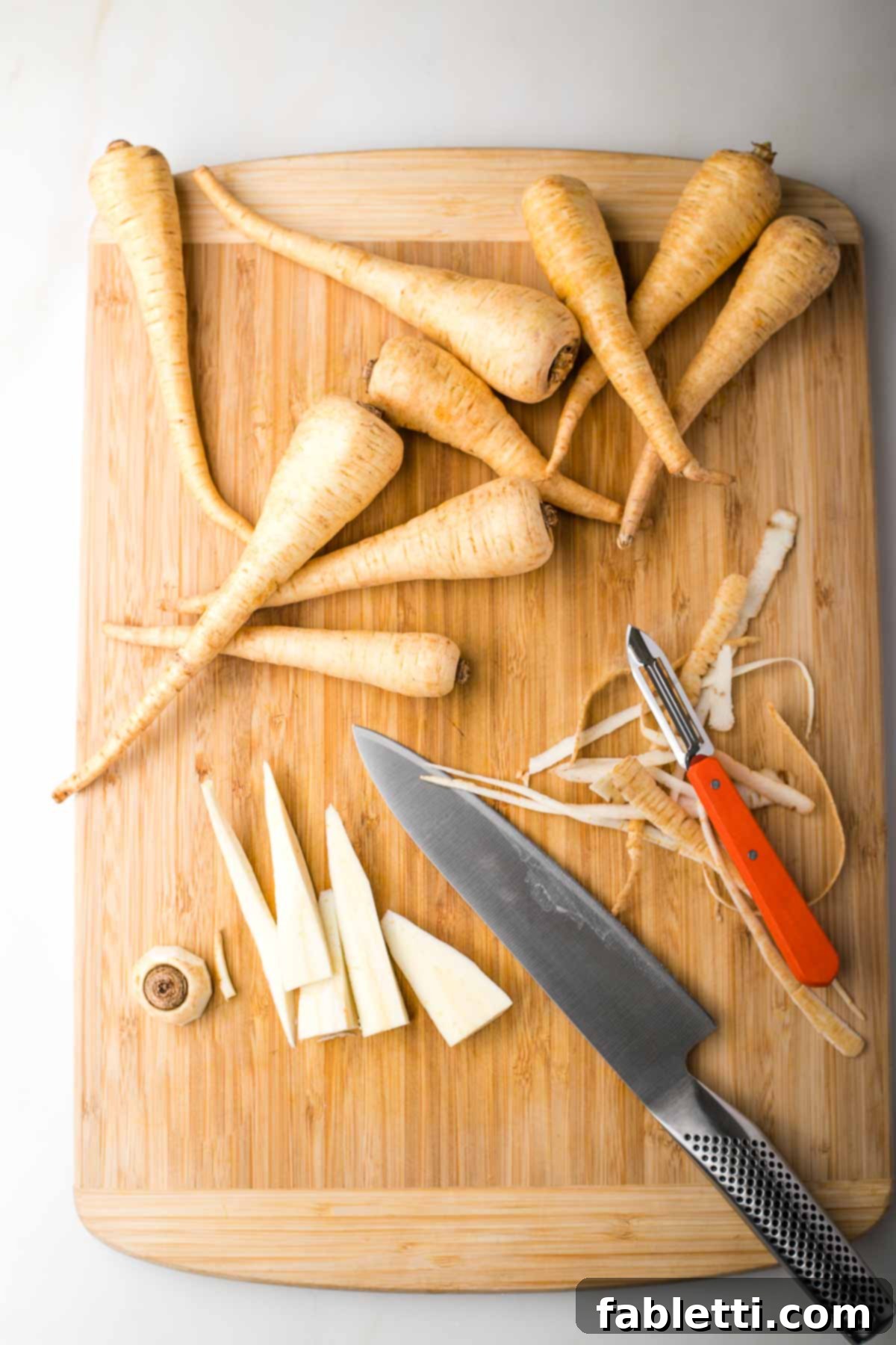 Nectar-Kissed Roasted Roots 4 Fresh parsnips on a cutting board. One is peeled and sliced lengthwise into thin strips.