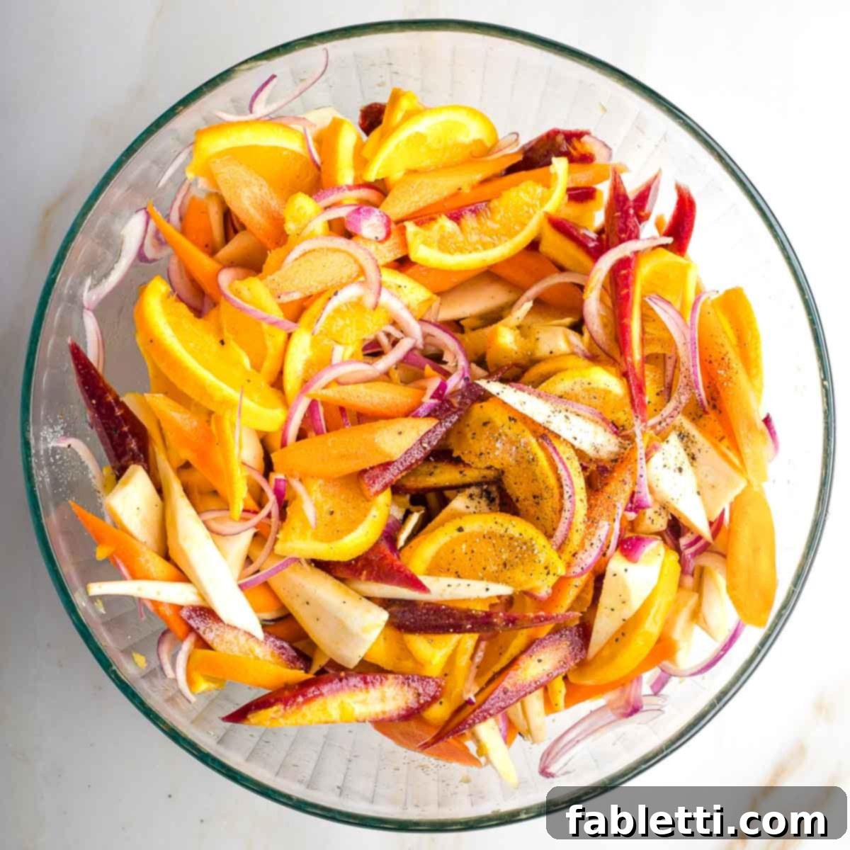 Nectar-Kissed Roasted Roots 7 Bowl of brightly colored carrots, parsnips, oranges and onions in a bowl, coated with the glaze.