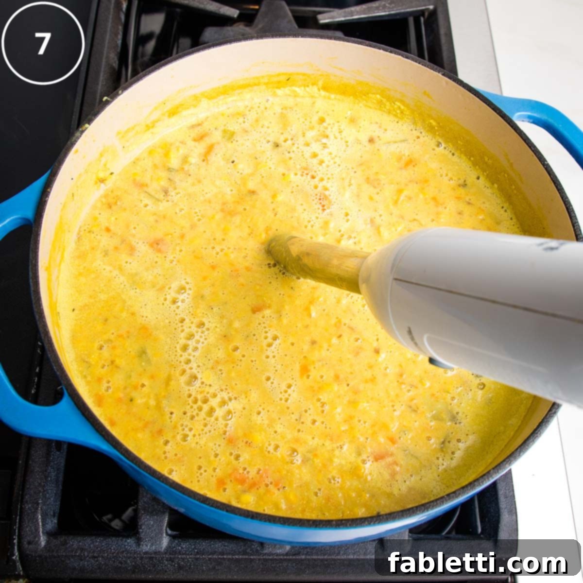 An immersion blender actively puréeing a portion of the corn chowder directly in the Dutch oven, creating a smooth, creamy base.