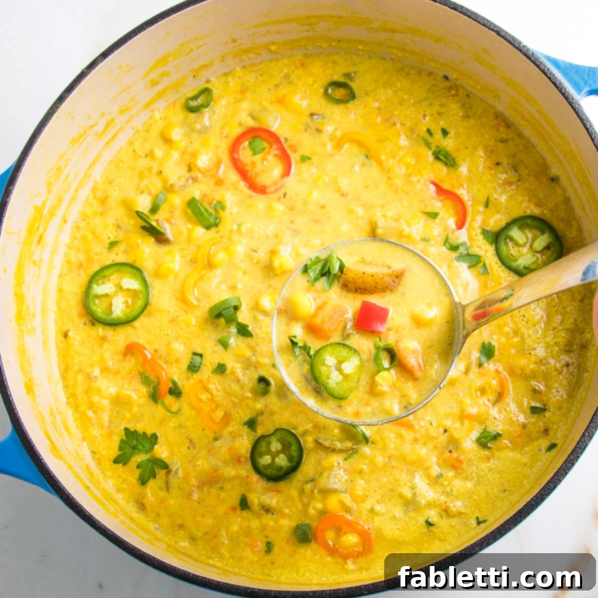 A Dutch oven brimming with finished corn chowder, garnished generously with colorful slices of mini bell peppers, fresh jalapeños, and fragrant herbs. The focus is on a ladle scooping up the rich, chunky chowder.