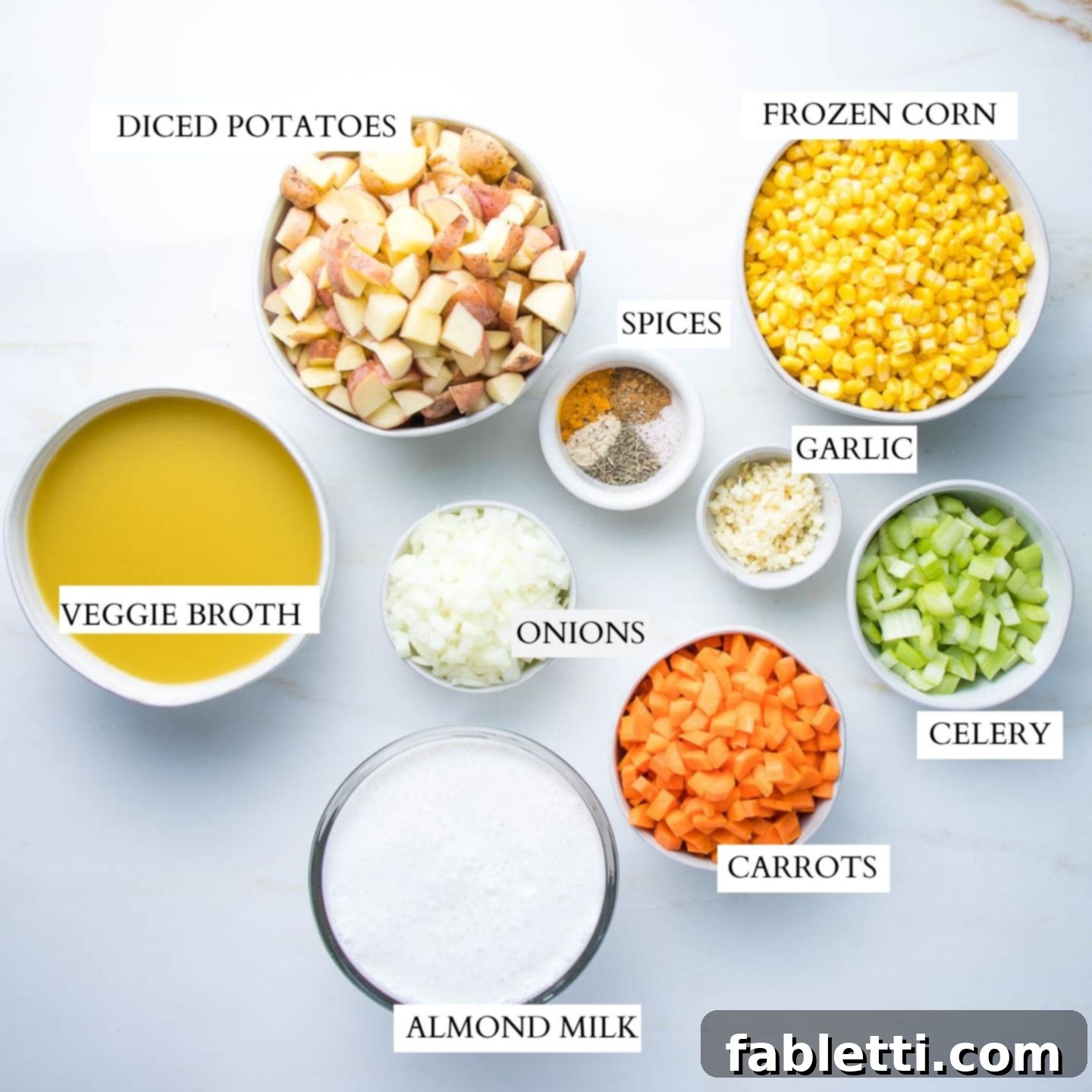 A vibrant flat lay showcasing all the essential ingredients for making delicious vegan corn chowder. Bowls filled with perfectly diced potatoes, golden frozen corn, a mix of aromatic spices, minced garlic, finely chopped onions, rich vegetable broth, creamy almond milk, bright carrots, and crisp celery are neatly arranged.