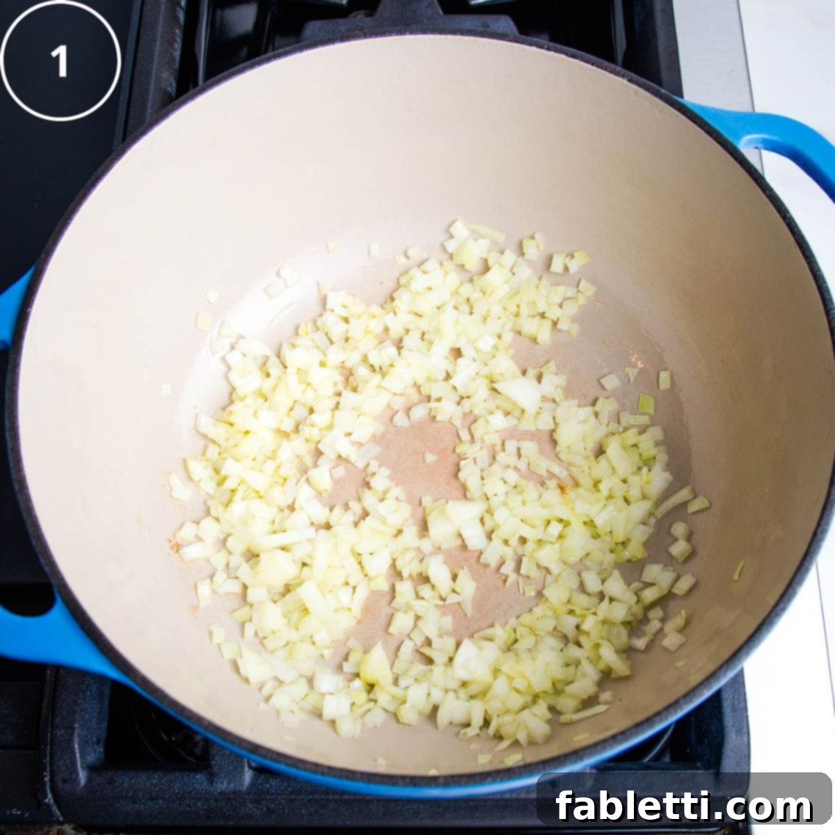 Diced onions being sautéed in a vibrant blue Dutch oven, shimmering gently as they begin to soften.
