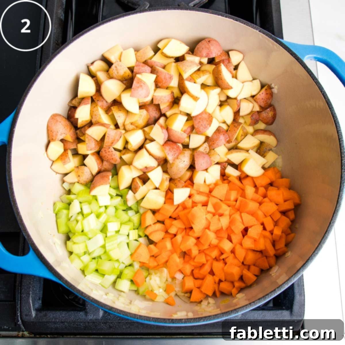 Diced carrots, celery, and potatoes added to a blue Dutch oven, mingling with the sautéed onions.