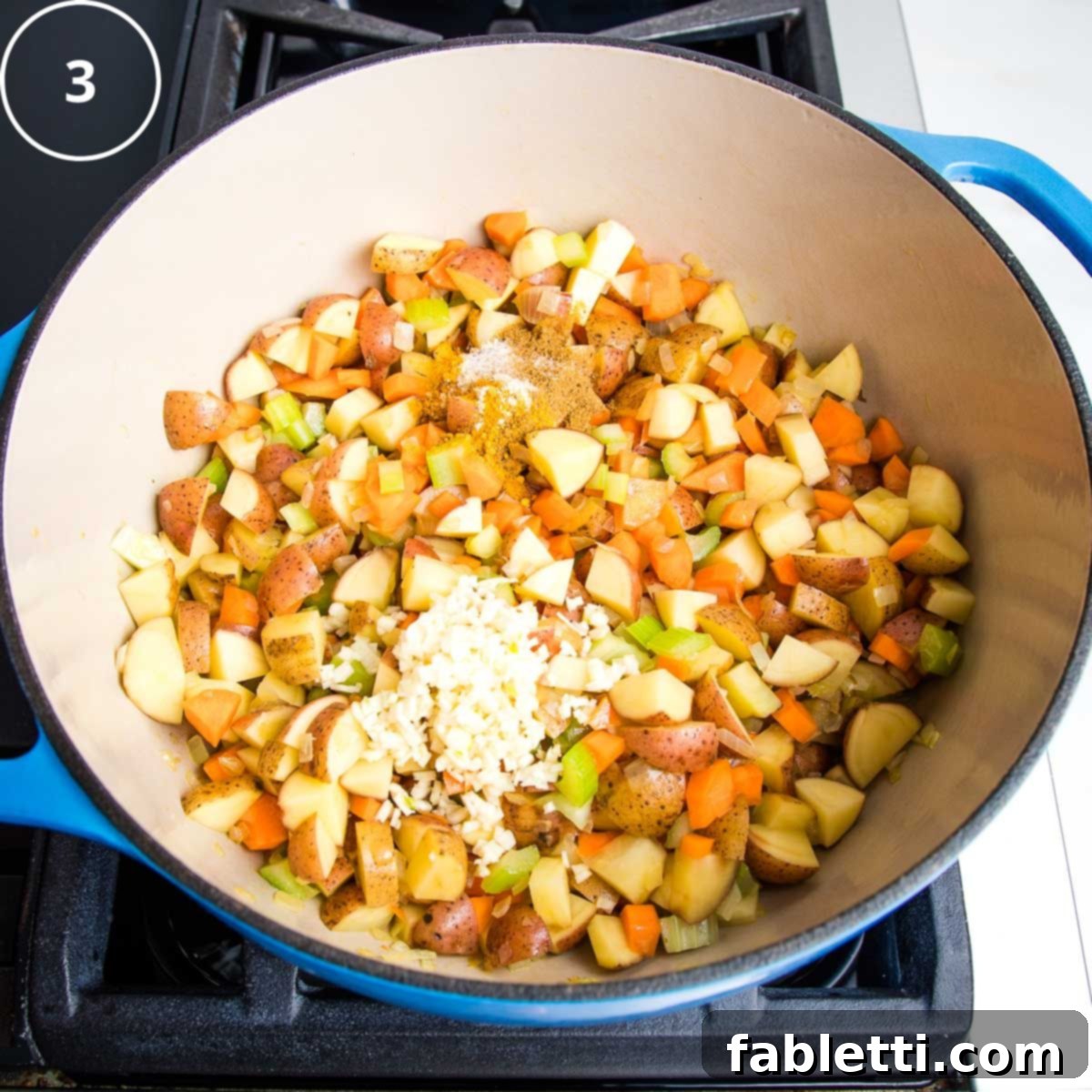 Sautéed carrots, potatoes, onions, and celery are now seasoned with a generous topping of minced garlic and a blend of aromatic spices, ready to be stirred.