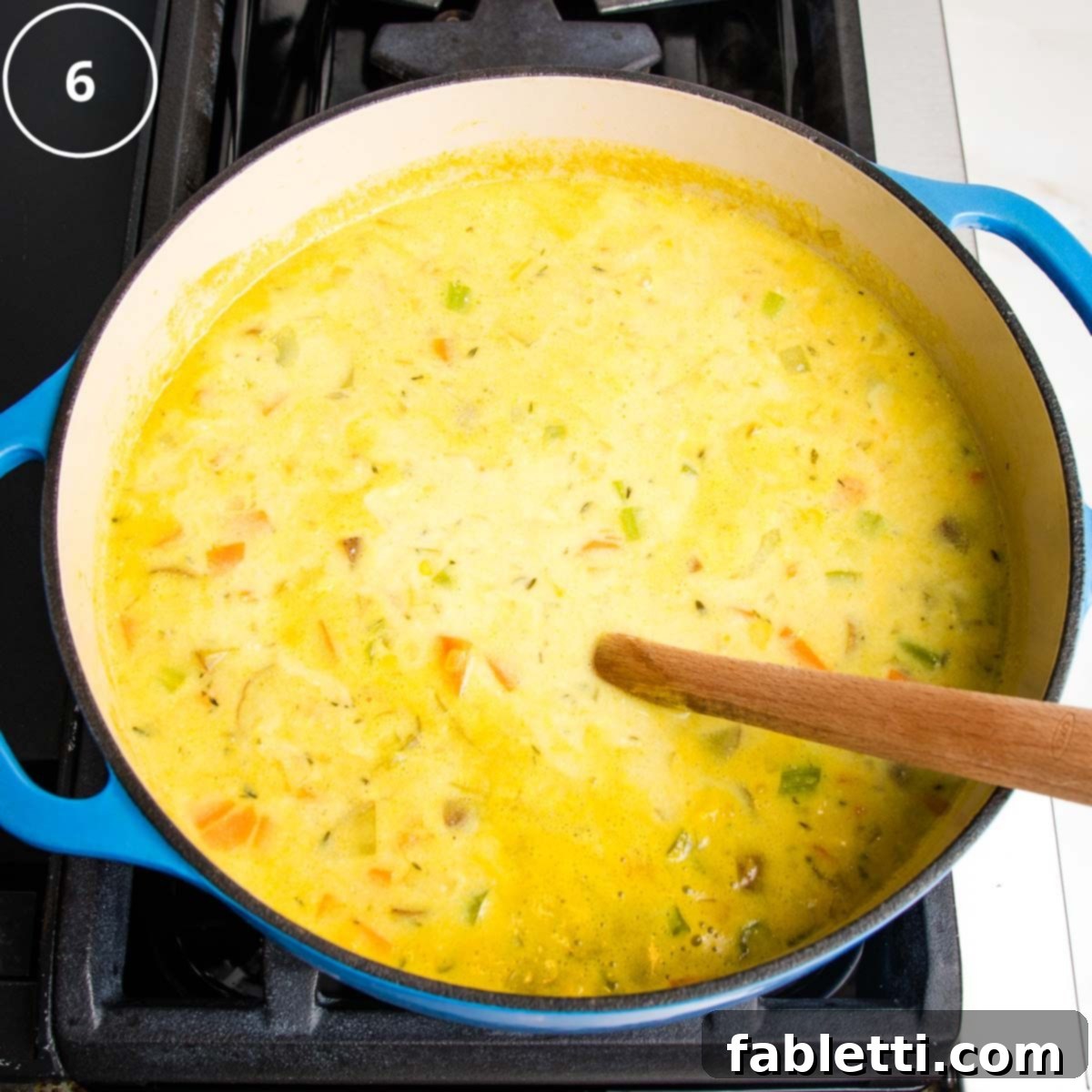 Creamy almond milk being stirred into the simmering yellow broth, filled with chunks of corn and vegetables, in a Dutch oven.