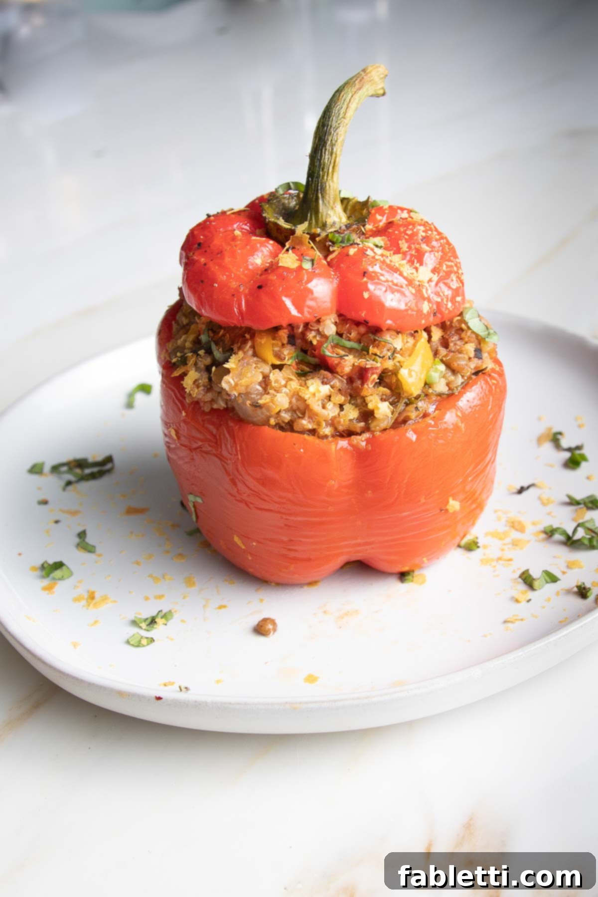 Hearty Vegan Lentil Stuffed Peppers 2 Red bell pepper stuffed with a flavorful quinoa and lentil mixture, garnished with fresh herbs.