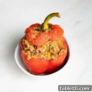 Hearty Vegan Lentil Stuffed Peppers 15 A red bell pepper stuffed with quinoa and lentils, garnished and ready to serve in a white bowl.