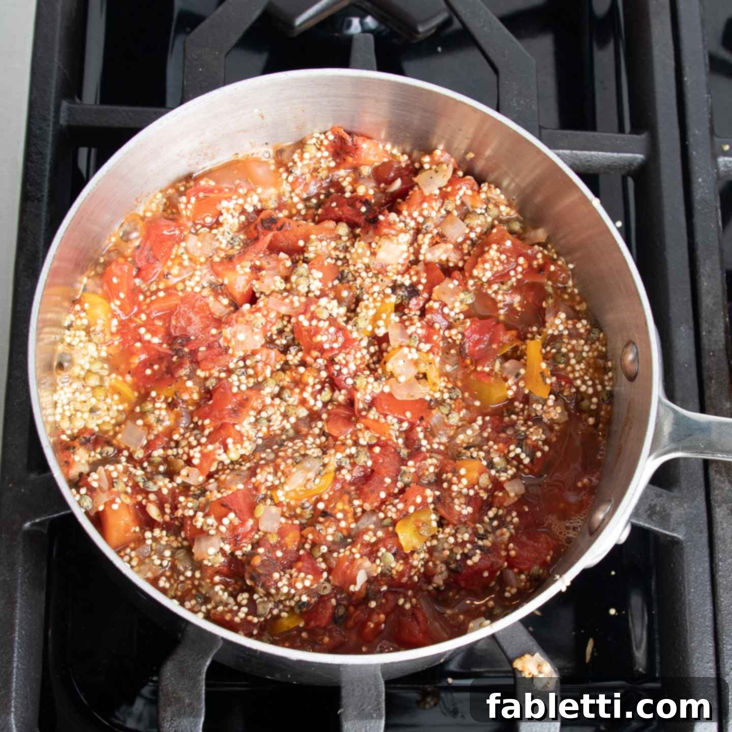 Hearty Vegan Lentil Stuffed Peppers 9 Cooked quinoa and lentils being mixed with diced tomatoes in a skillet.