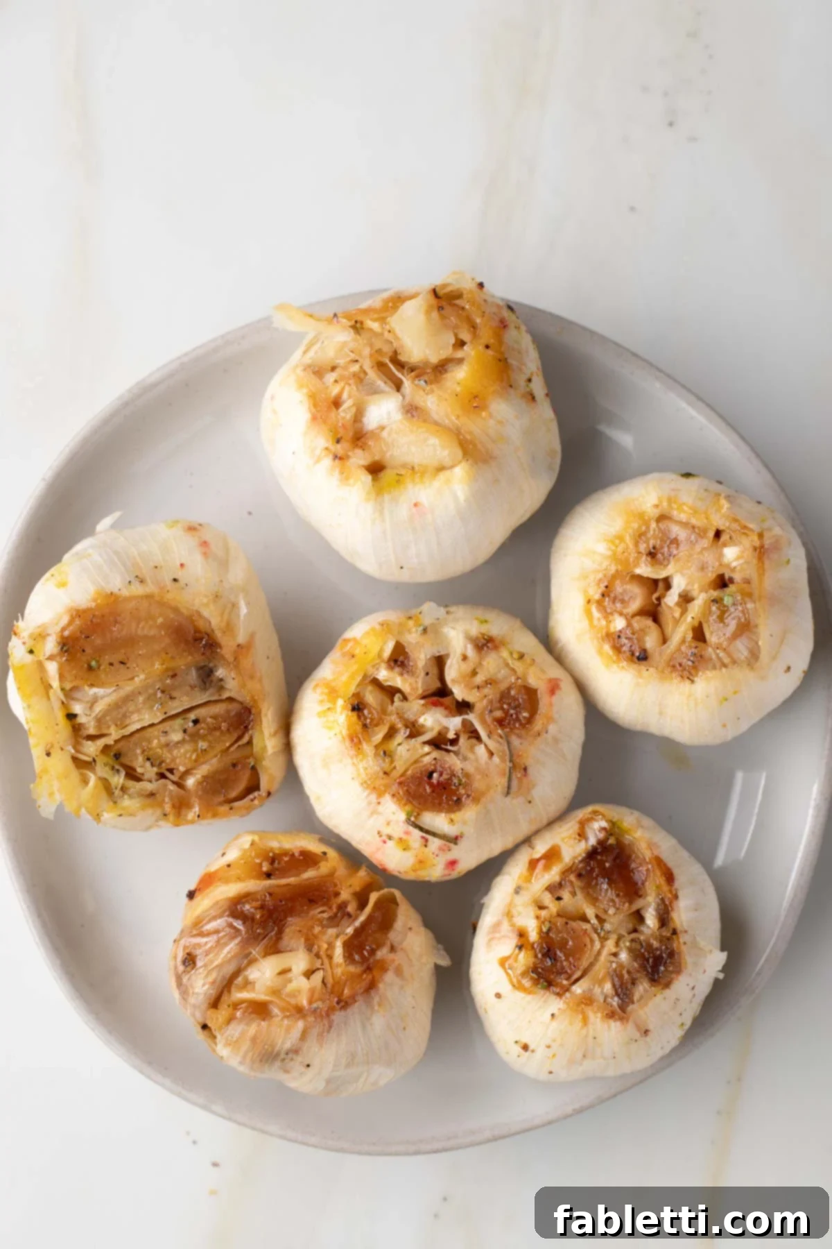 Sweet Creamy Oven Roasted Garlic 2 Golden brown whole roasted bulbs of garlic resting on a plate, ready to be enjoyed.