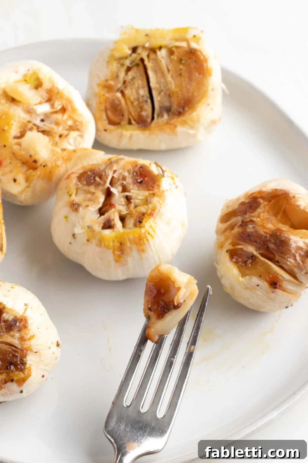 Sweet Creamy Oven Roasted Garlic 11 A single, perfectly golden-brown roasted garlic clove being pulled from its bulb.