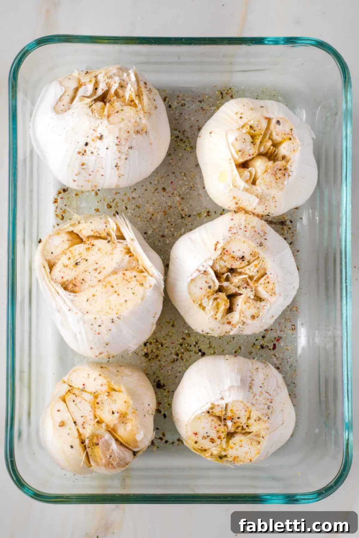 Sweet Creamy Oven Roasted Garlic 5 Six whole heads of garlic in a baking dish, drizzled with olive oil and sprinkled with salt and black pepper.