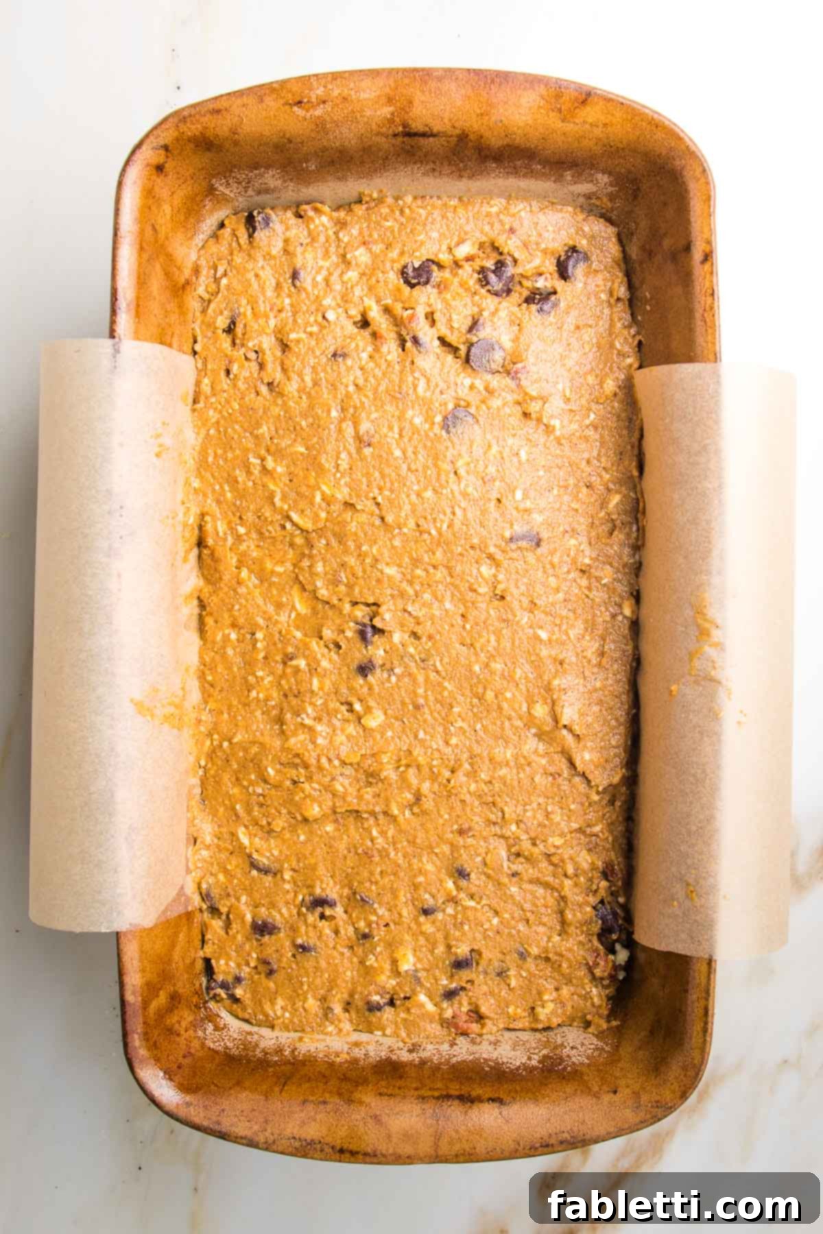 Harvest Spice Vegan Banana Loaf 6 Pumpkin bread batter meticulously poured into a loaf pan, perfectly lined with parchment paper, showcasing the rich texture before baking.