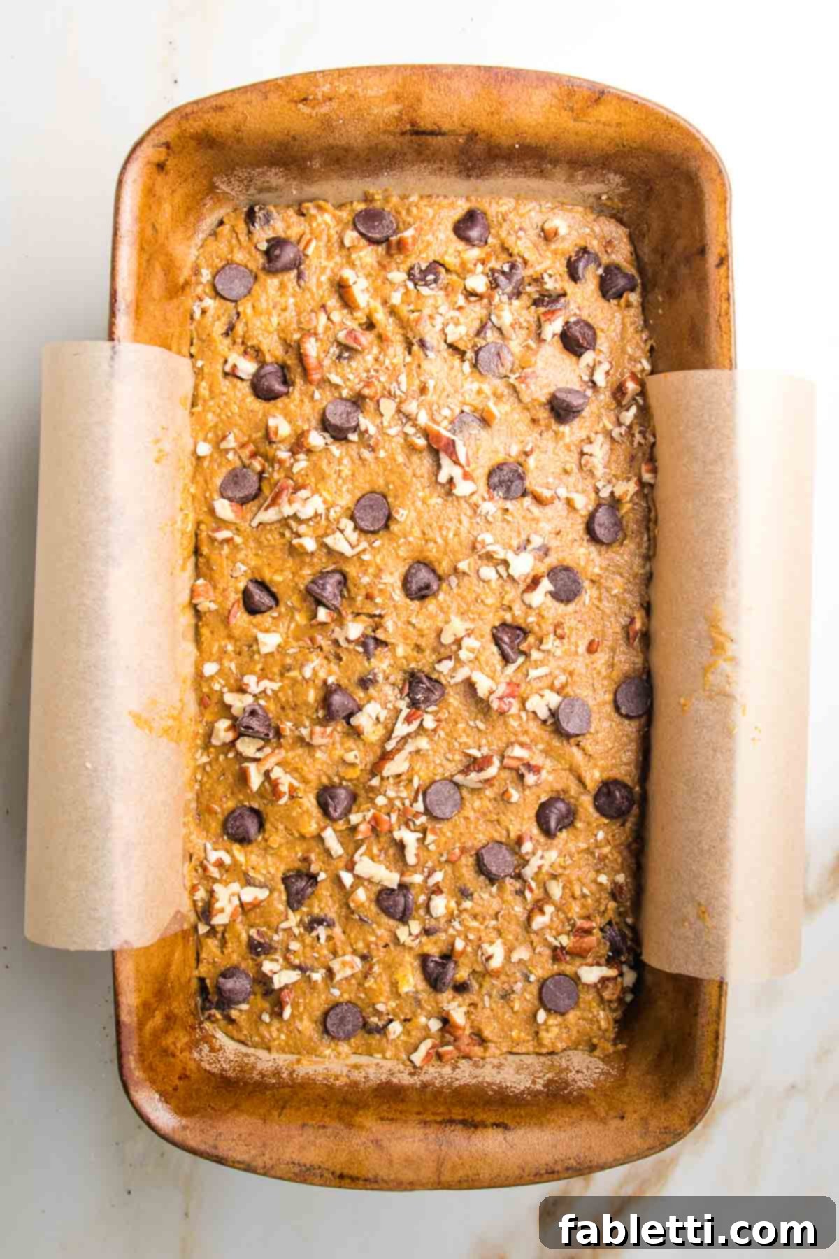 Harvest Spice Vegan Banana Loaf 7 The vegan pumpkin bread batter in a parchment-lined loaf pan, generously topped with an inviting sprinkle of chocolate chips and chopped pecans, ready for the oven.