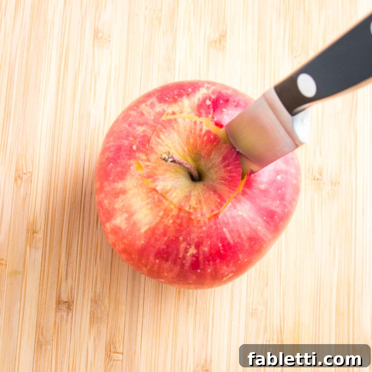 Naturally Sweet Dairy-Free Baked Apples 7 Close up of a honeycrisp apple on a cutting board with a small paring knife inserted on the top for removing the core, illustrating a precise and controlled coring technique.