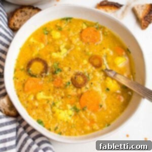 Large white bowl filled with thick and creamy red lentil soup that also has chunks of cauliflower and carrots.