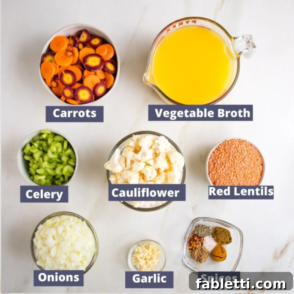 Labeled ingredients for the soup: Fresh, vibrant carrots, rich vegetable broth, crisp celery, florets of cauliflower, nutritious red lentils, a pungent onion, aromatic garlic, and a selection of fragrant spices.