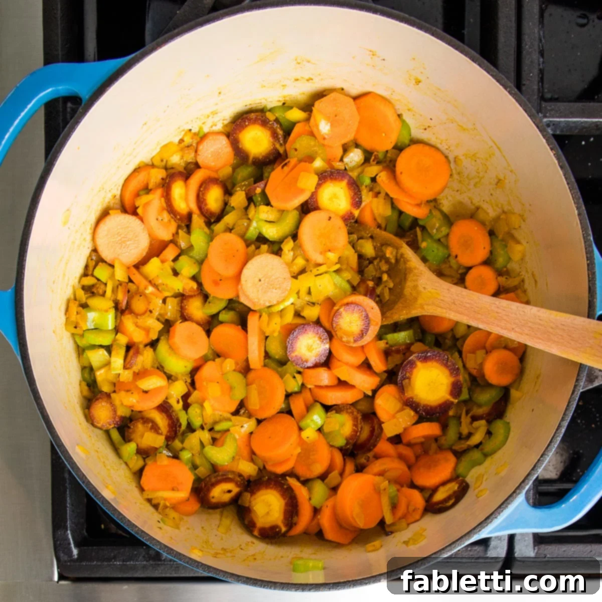 An assortment of brightly colored vegetables, including orange and purple carrots and crisp celery, are gently cooking with fragrant spices in a Dutch oven, gradually softening and releasing their aromas.