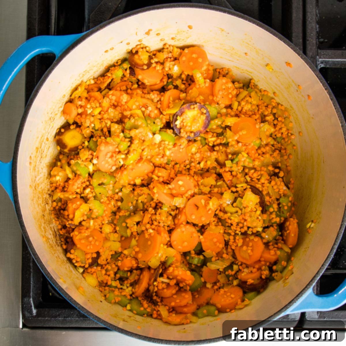 The Dutch oven now contains gently sweated vegetables, beautifully coated in spices, with a generous addition of vibrant red lentils, ready to absorb more flavor.
