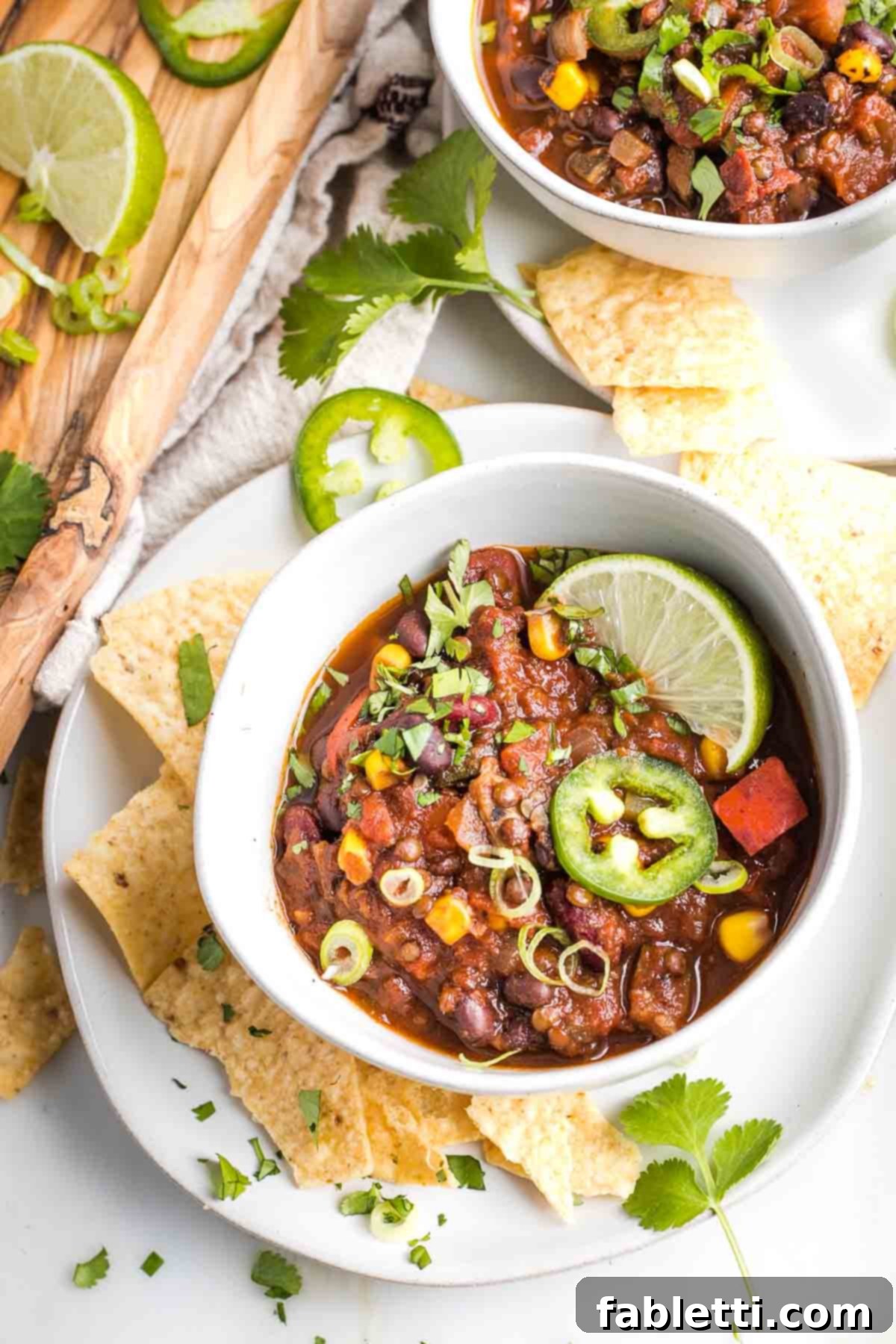 Quick and Flavorful Vegan Lentil Chili 2 A vibrant bowl of easy vegan chili, generously topped with fresh cilantro, a slice of fiery jalapeño, a lime wedge, and crispy corn chips. The chili itself is rich with lentils, beans, and corn.